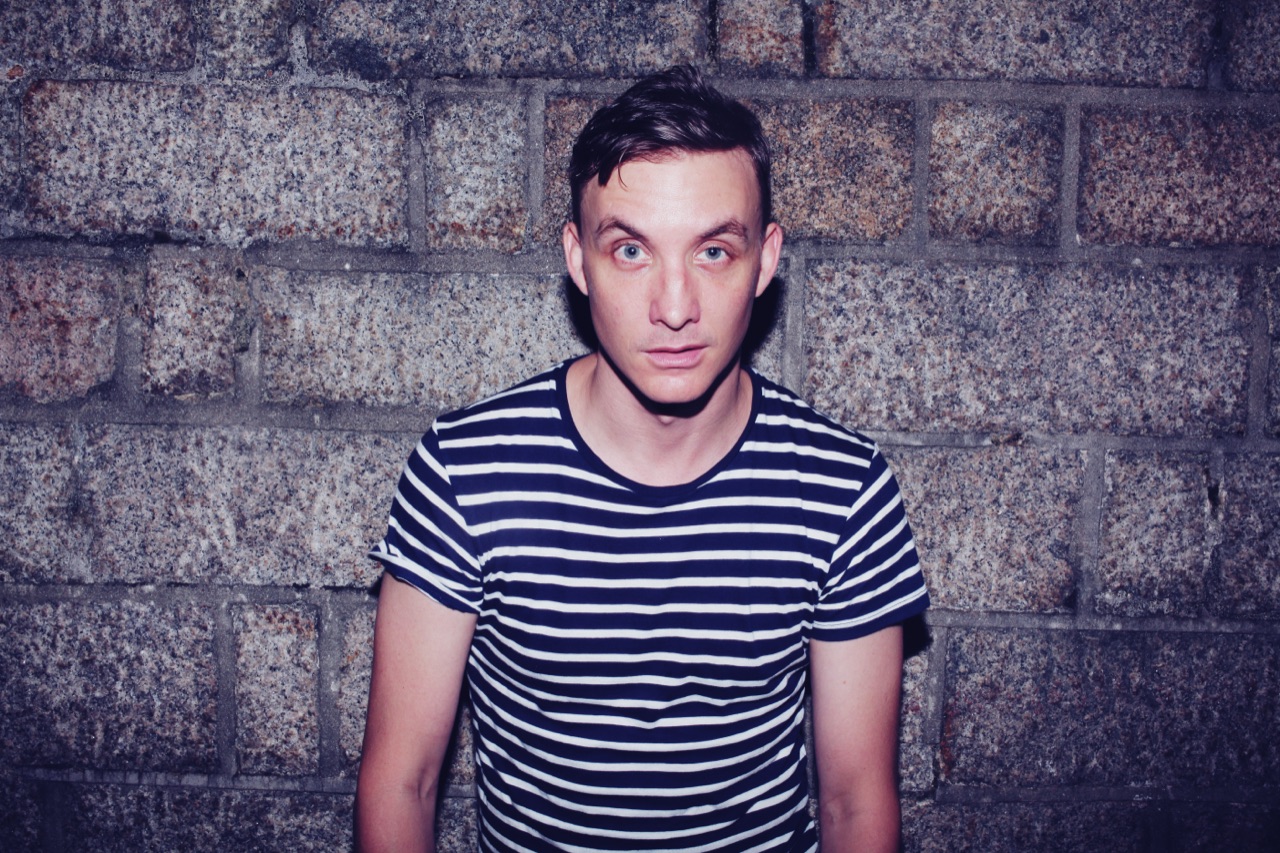 DJ Ryan Ash portrait in a striped t-shirt against a granite wall