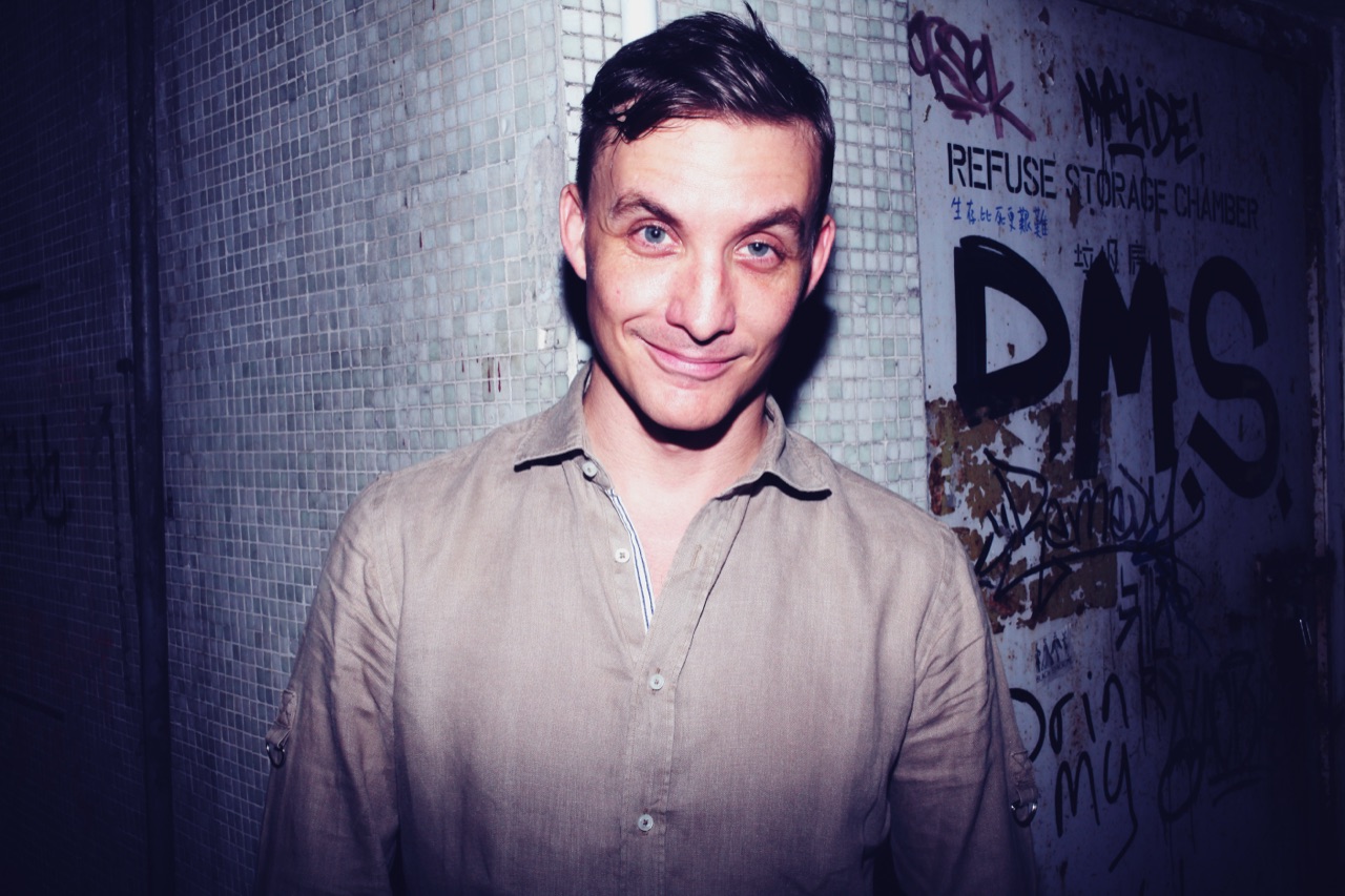 DJ Ryan Ash smiling against a tiled Hong Kong backstreet wall